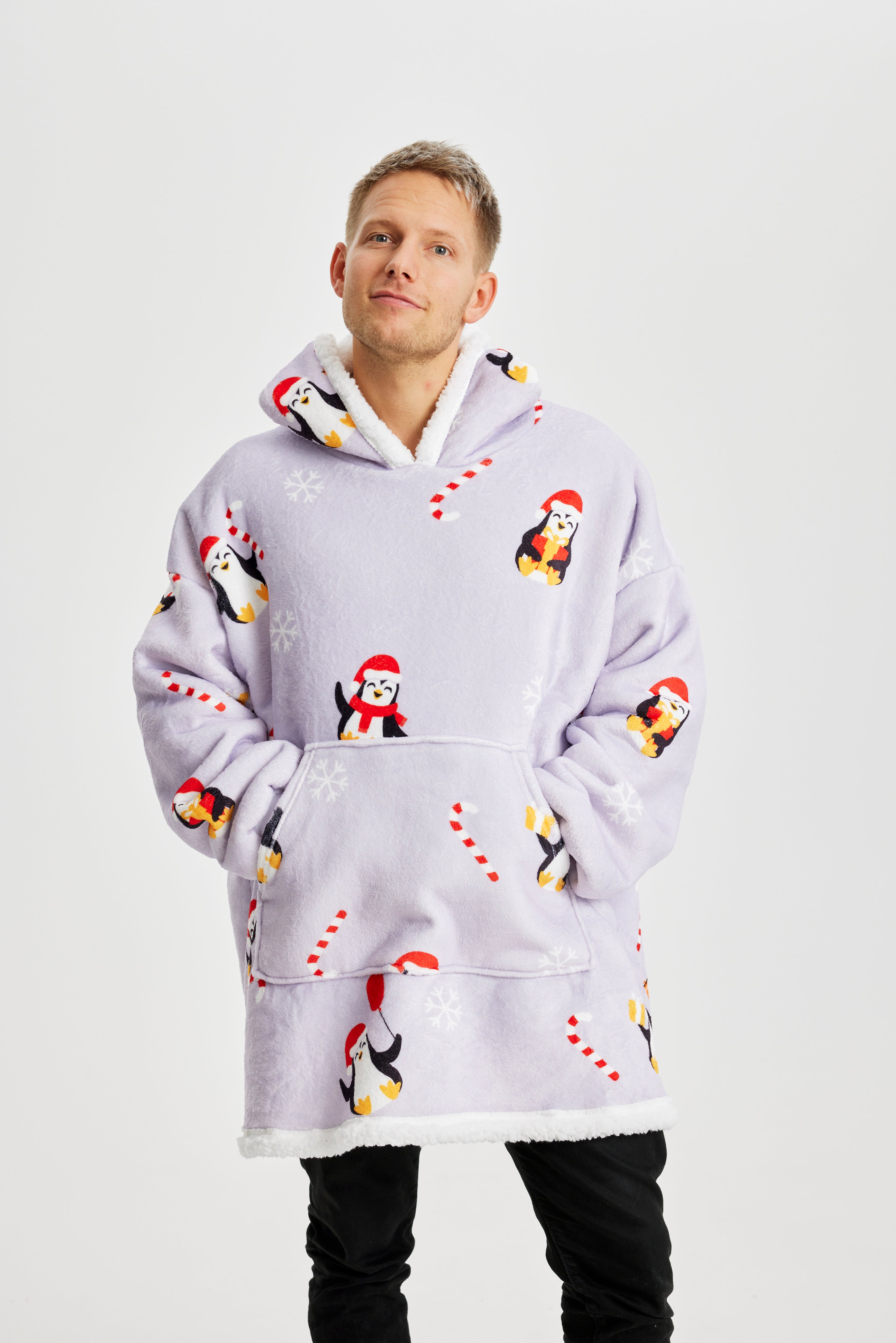 Un homme, les mains dans les poches, portant un sweat à capuche de Noël violet clair avec des pingouins dessus.